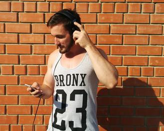 Hipster im Hemd hlt hochwertiges Handy mit Headphone hoch. (Pixabay)